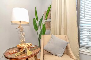 Ein Eckzimmer mit Lampe, einem Sessel, einem Tisch mit Dekoration und einer großen Pflanze.