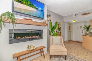 Ein Wohnzimmer mit Fernseher, Kamin, Sitzbank und einer Tür zum Küchenbereich.