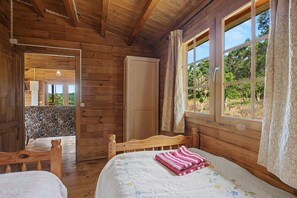 Una habitación de cabaña de madera con una cama, una silla, un armario y un ventanal con cortinas.