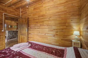 Una habitación con paneles de madera, una cama, una mesita de noche y una puerta que da a otra estancia.