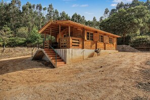 A wooden cabin with a staircase leading to a porch, surrounded by trees.
