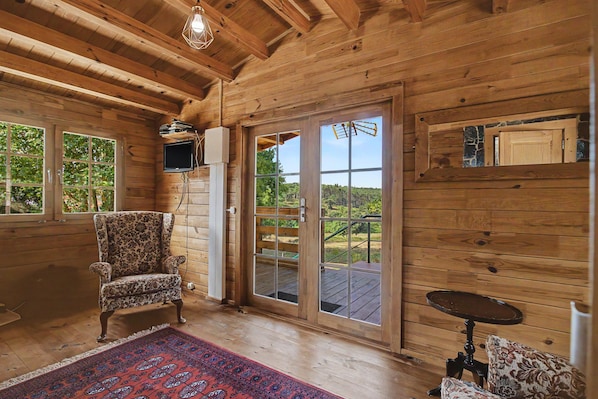 A wooden interior with a large sliding glass door, a chair, a small table, and a mounted television.