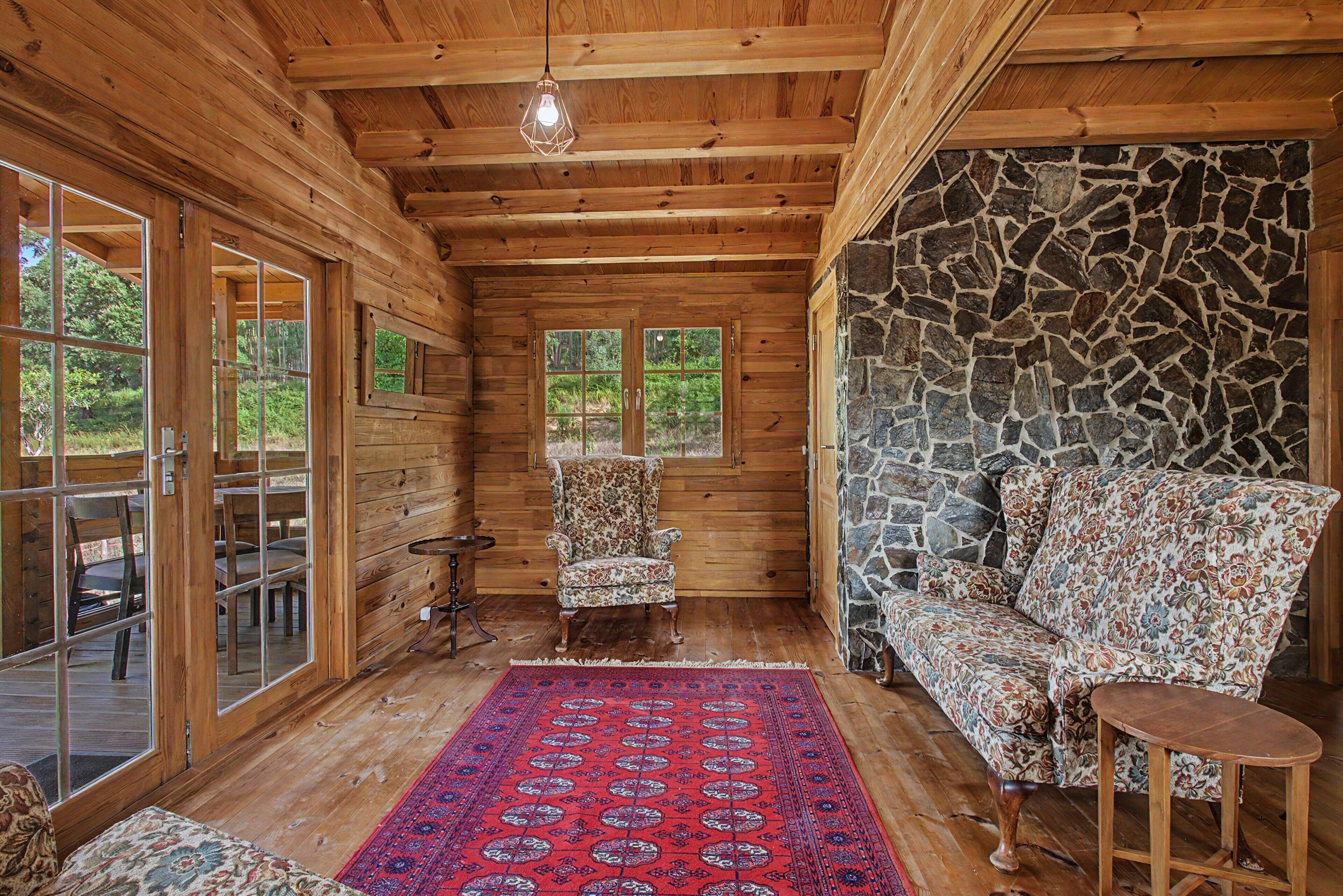 A log cabin interior with a stone wall, a patterned rug, and a floral sofa.