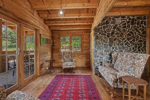 Interior de una cabaña de troncos con una pared de piedra, un tapete estampado y un sofá floral.