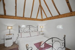 A bedroom with a four-poster bed, two bedside tables, a nightstand, and a sloped ceiling with exposed wooden beams.