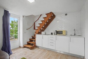 A kitchen with a wooden staircase, white cabinets, a microwave, and a window with curtains.