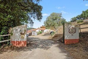 A rural entrance with a dirt path leading to a building with a tiled roof.