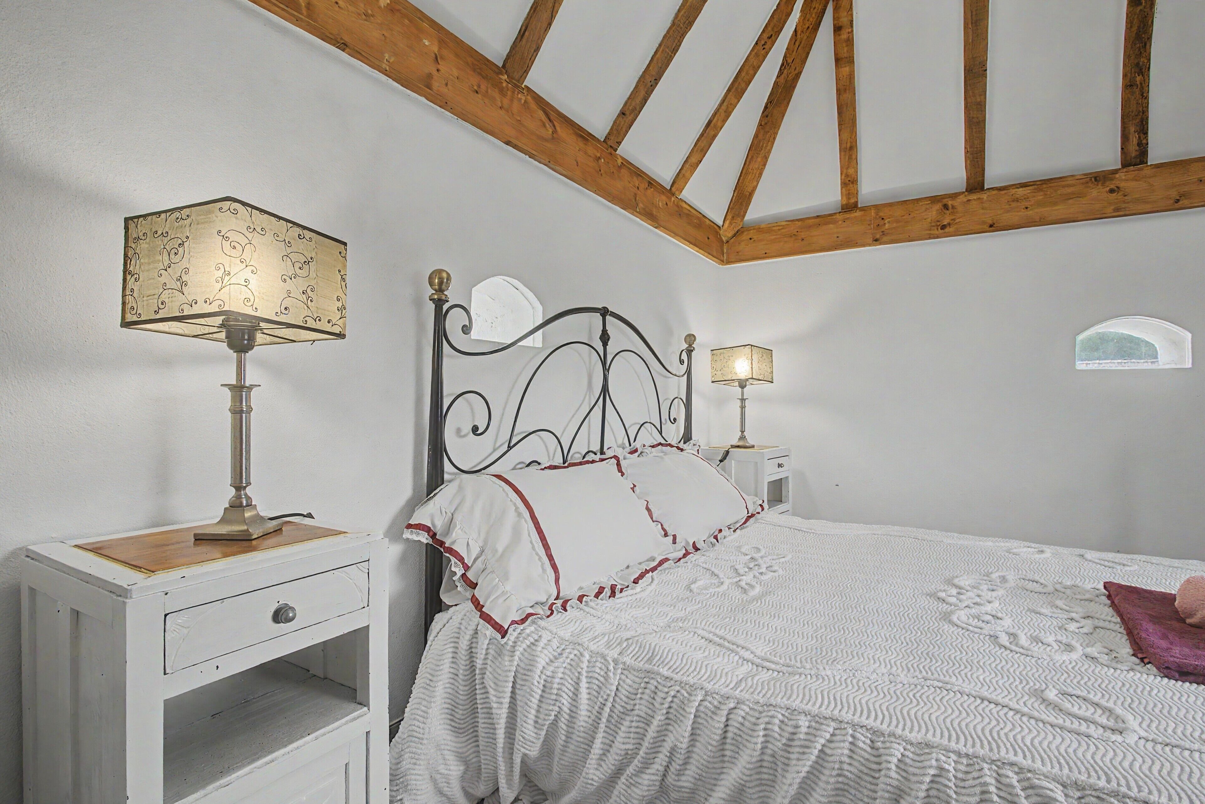 Een slaapkamer met een bed, twee nachtkastjes, een lamp en een houten plafond.
