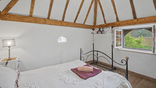 Une chambre à coucher avec un lit, une fenêtre donnant sur un beau paysage, une lampe et une petite étagère fixée au mur.