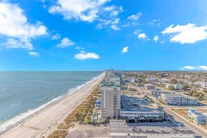 A coastal cityscape with a beach, a tall hotel, and a clear blue sky. - Palace 1909 Ocean View Studio (Myrtle Beach)