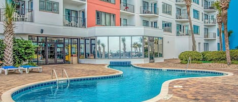 A hotel with a swimming pool, a covered area, and a multi-story building with balconies.