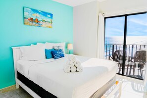 A hotel room with a bed, a painting, a balcony with chairs, and a view of the sea. - Palace 1909 Ocean View Studio (Myrtle Beach)
