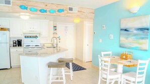 A kitchen with white cabinets, a stove, and a sink. There is a dining area with a table and chairs. - Palace 1909 Ocean View Studio (Myrtle Beach)