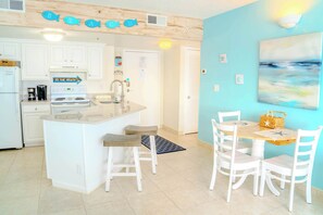 A kitchen with white cabinets, a stove, and a sink. There is a dining area with a table and chairs. - Palace 1909 Ocean View Studio (Myrtle Beach)
