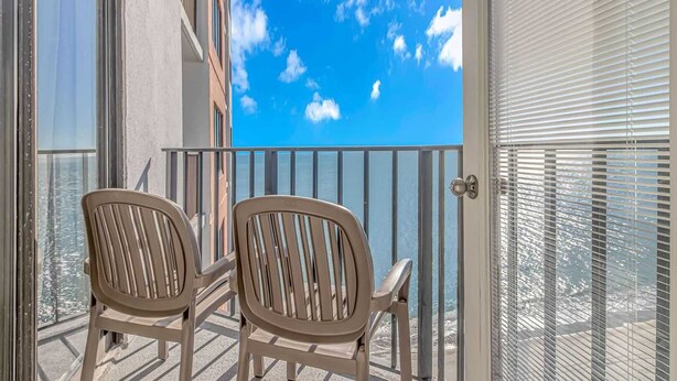 A balcony with two chairs, a metal railing, and a view of the sky and water. - Palace 1909 Ocean View Studio (Myrtle Beach)