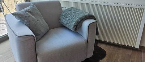 Ein hellgraues Sofa mit Decke und Kissen, ein dunkelbrauner Shag-Teppich und ein weißer Heizkörper in einem Raum mit Holzboden.