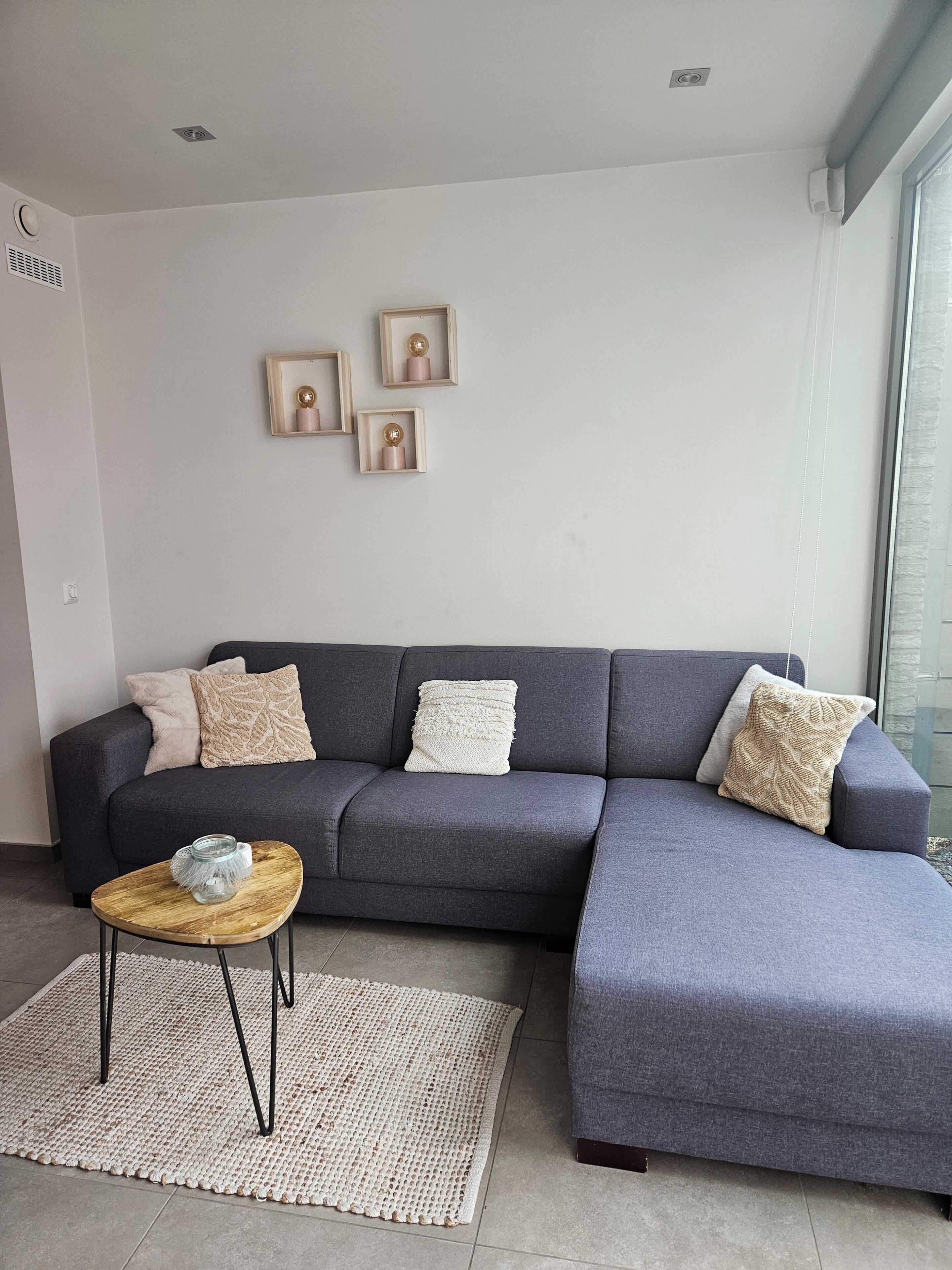 Ein modernes Wohnzimmer mit einem grauen Ecksofa, einem kleinen Holztisch und einem gewebten Teppich.
