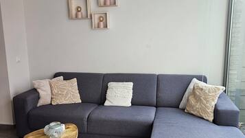 Ein modernes Wohnzimmer mit einem grauen Ecksofa, einem kleinen Holztisch und einem gewebten Teppich.