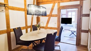 A dining area with a round table, chairs, a vase with flowers, and a hanging lamp. - Heinrich Apartment in a half-timbered house from 1596 – Jena’s Old Town (Jena)