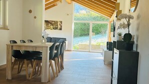 Un'ampia stanza con un tavolo e sedie di legno, un mobile contenitore nero e un'ampia finestra che si affaccia sul verde.
