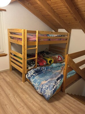Una cama litera con estructura de madera, la litera inferior con un edredón colorido y un techo con vigas de madera a la vista.