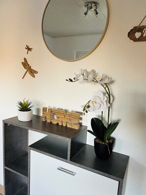 A modern room with a desk, a mirror, a potted plant, decorative wooden letters spelling 'HOME,' and a wall-mounted fan.