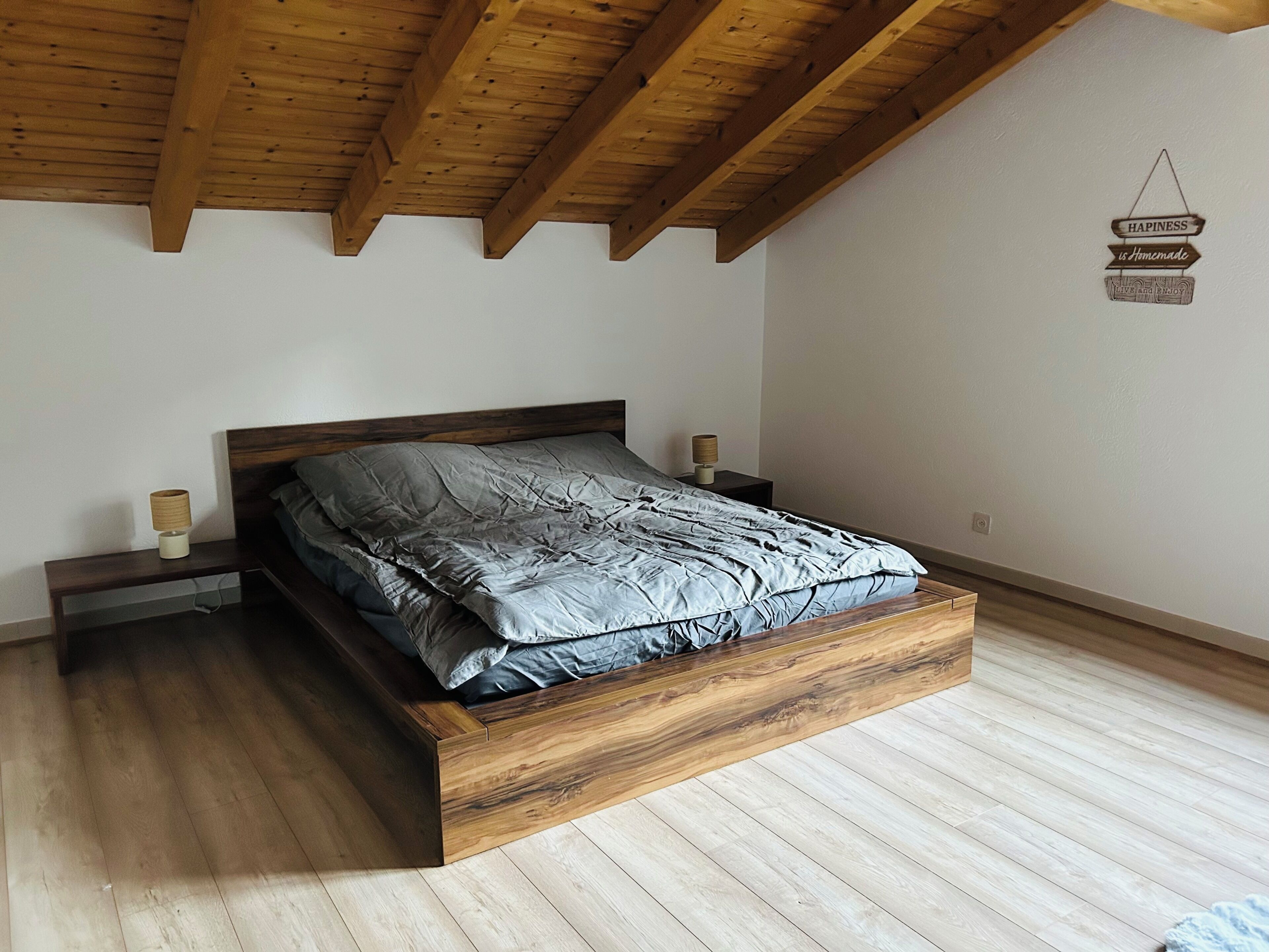 Een slaapkamer met een houten bedframe, een nachtkastje met een lamp en een bordje aan de muur.
