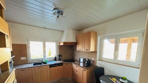 Una cucina compatta con mobili in legno, lavastoviglie integrata, macchina del caffè e un piccolo tavolo da pranzo con una sedia.