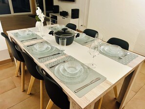 Una mesa de comedor dispuesta con cubertería, platos y copas de cristal, rodeada de sillas negras.