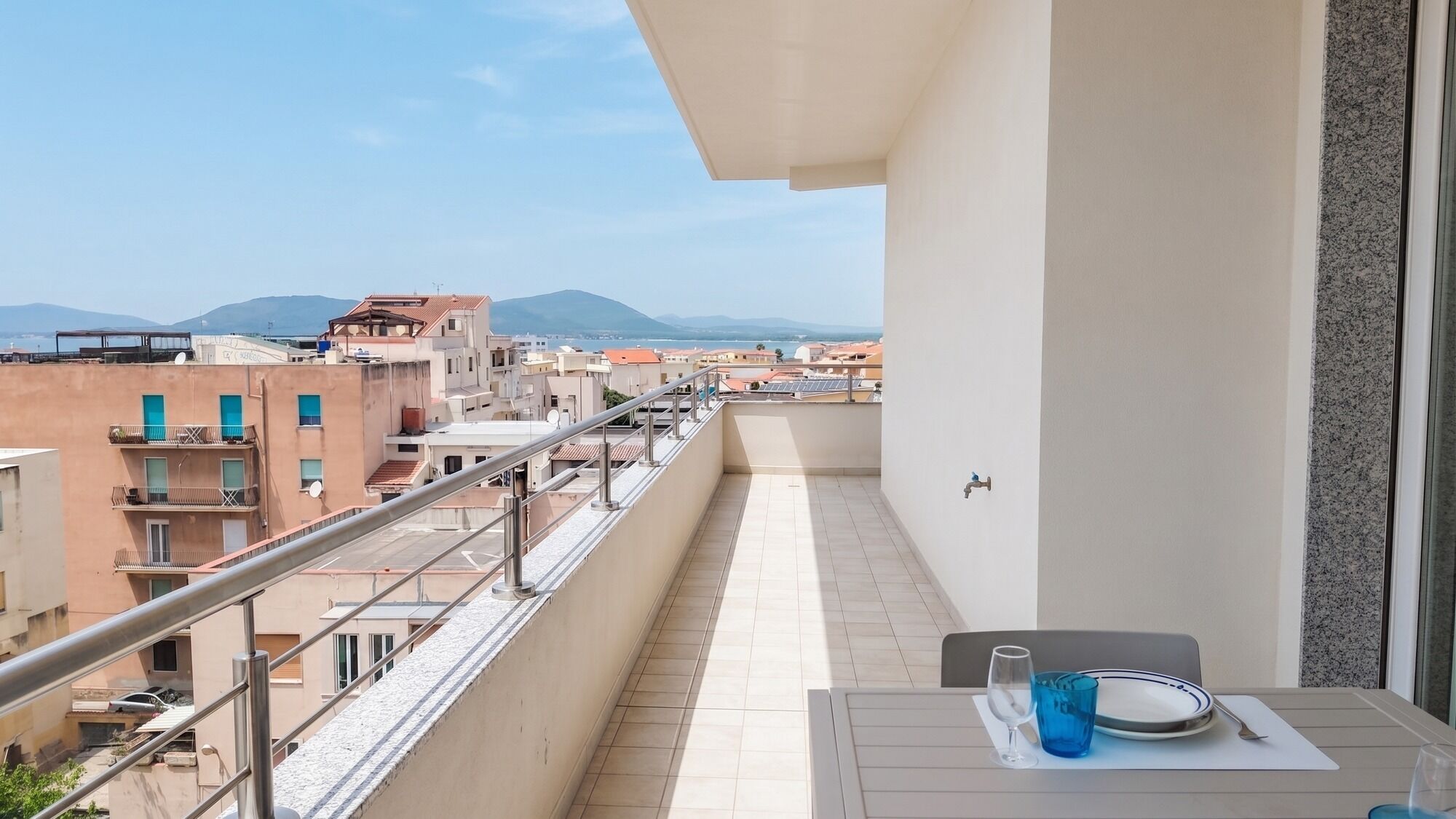 En balkon med et bord dækket til to, der vender ud mod et bybillede med bygninger og fjerne bjerge.