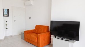 A living room with a large flat-screen TV, a white door, and a small orange chair. - Sunset Panorama - Two Bedroom Apartment, Sleeps 4 (Alghero)