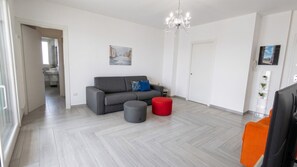 A modern living room with a grey sofa, a red ottoman, and a chandelier. - Sunset Panorama - Two Bedroom Apartment, Sleeps 4 (Alghero)