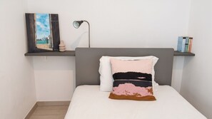 A bedroom with a bed, a bedside lamp, a shelf with books, and a wall-mounted picture. - Sunset Panorama - Two Bedroom Apartment, Sleeps 4 (Alghero)