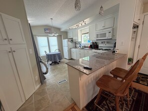 A kitchen with white cabinets, a granite countertop, and a dining area with a table and chairs. - Outdoorsman's hunting-fishing 2-bedroom oasis near Pleasanton Kansas. (Pleasanton)