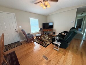 A living room with hardwood floors, a television, a rocking chair, a sofa, and a patterned rug. - Outdoorsman's hunting-fishing 2-bedroom oasis near Pleasanton Kansas. (Pleasanton)