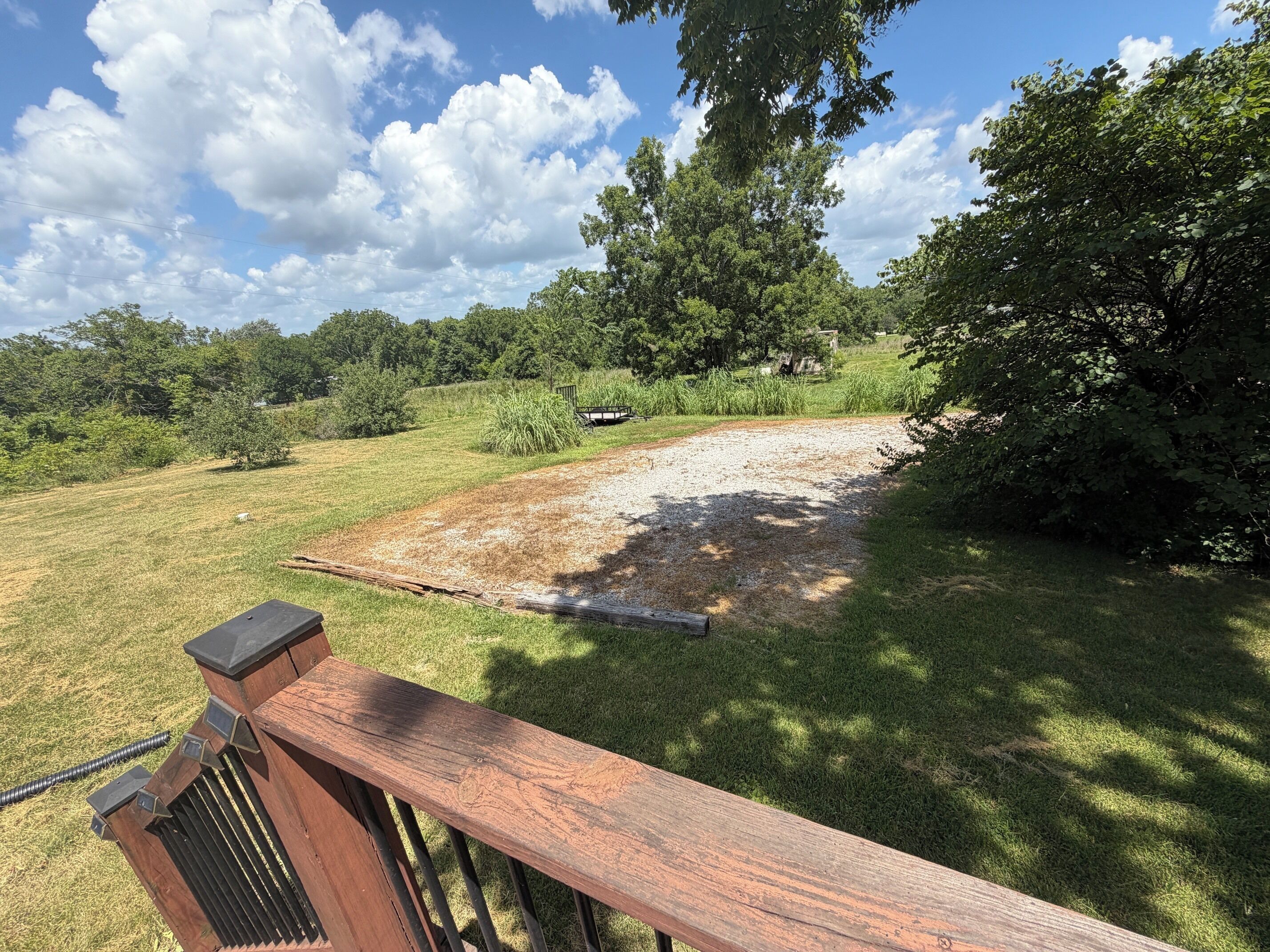 A wooden deck with a metal railing, a gravel area, and trees in the background.