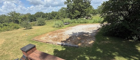 A wooden deck with a metal railing, a gravel area, and trees in the background.