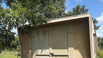 A small, single-story wooden structure with a door and windows, surrounded by grass and trees.