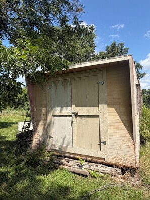 A small, single-story wooden structure with a door and windows, surrounded by grass and trees. - Outdoorsman's hunting-fishing 2-bedroom oasis near Pleasanton Kansas. (Pleasanton)
