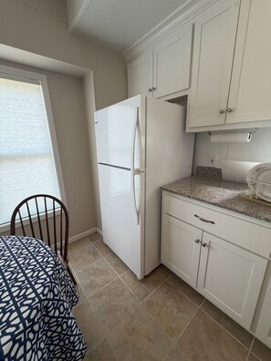 A kitchen with white cabinets, a white refrigerator, a granite countertop, and a chair with a patterned tablecloth. - Outdoorsman's hunting-fishing 2-bedroom oasis near Pleasanton Kansas. (Pleasanton)