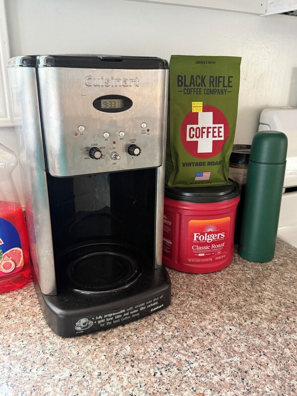 A Cuisinart coffee maker on a kitchen counter with a bag of Folgers coffee and a green thermos.