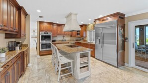 A kitchen with wooden cabinets, a stainless steel refrigerator, a built-in oven, and a granite countertop. - LUXE Waterfall Pool w/ Fire Cave, Private 2+ Acre Riverfront Estate, Pickleball (Merritt Island)