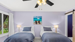 A bedroom with two beds, a ceiling fan, a beach-themed wall art, and a view of the outdoors. - LUXE Waterfall Pool w/ Fire Cave, Private 2+ Acre Riverfront Estate, Pickleball (Merritt Island)
