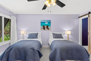 Ein Schlafzimmer mit zwei Betten, einem Deckenventilator, einer Wanddekoration zum Thema Strand und Blick ins Freie.