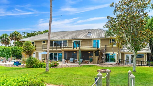 A two-story house with a balcony, a swimming pool, and a well-maintained lawn. - LUXE Waterfall Pool w/ Fire Cave, Private 2+ Acre Riverfront Estate, Pickleball (Merritt Island)