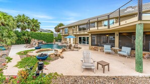 A two-story building with a swimming pool, outdoor seating, and a landscaped garden. - LUXE Waterfall Pool w/ Fire Cave, Private 2+ Acre Riverfront Estate, Pickleball (Merritt Island)
