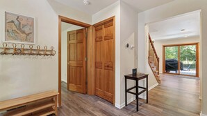 Un pasillo amplio con piso de madera, una puerta de madera, un perchero, una pequeña mesa y una escalera que conduce a un balcón.