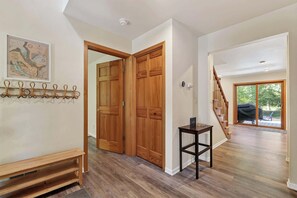 A spacious hallway with wooden flooring, a wooden door, a coat rack, a small table, and a staircase leading to a balcony. - Dog Friendly Home in Sturgeon Bay with fire pit (Sturgeon Bay)