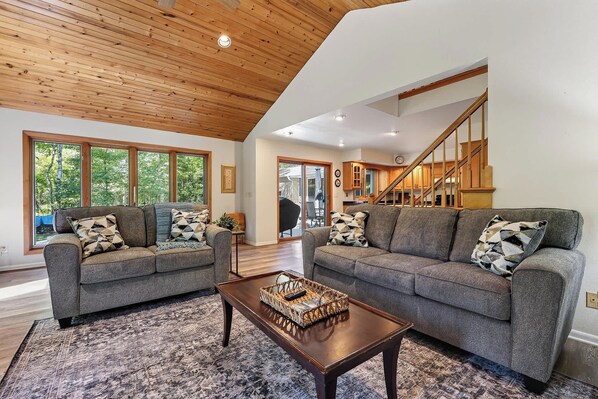 A modern living room with two grey sofas, a wooden coffee table, and a large window offering a view of trees. - Dog Friendly Home in Sturgeon Bay with fire pit (Sturgeon Bay)