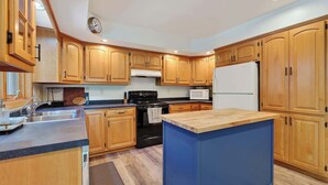 Una cocina con armarios de madera, estufa negra, refrigerador blanco e isla azul.